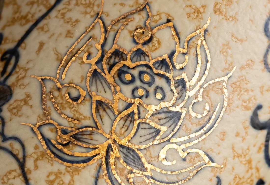 Macro photograph of the cup’s hand-painted trailing lotus with raised gold-colored outlines and cobalt-blue brushwork