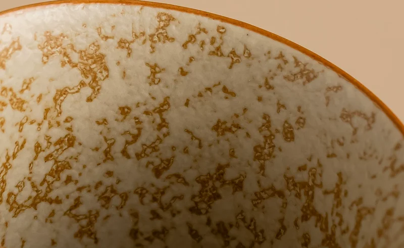 Close-up of the porcelain cup’s mottled glaze and gold-colored rim